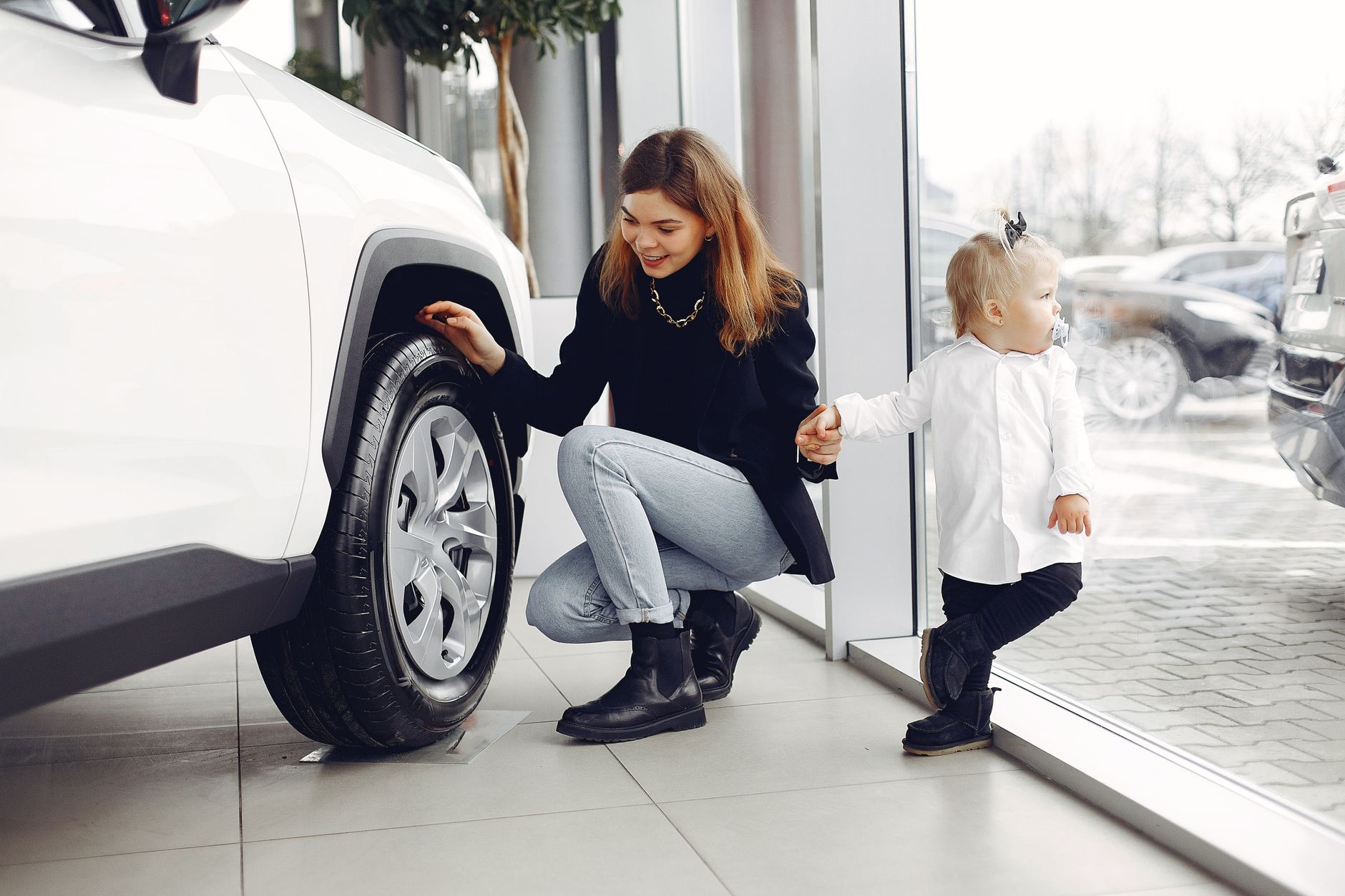 Mãe e criança observando o pneu de um carro em uma concessionária